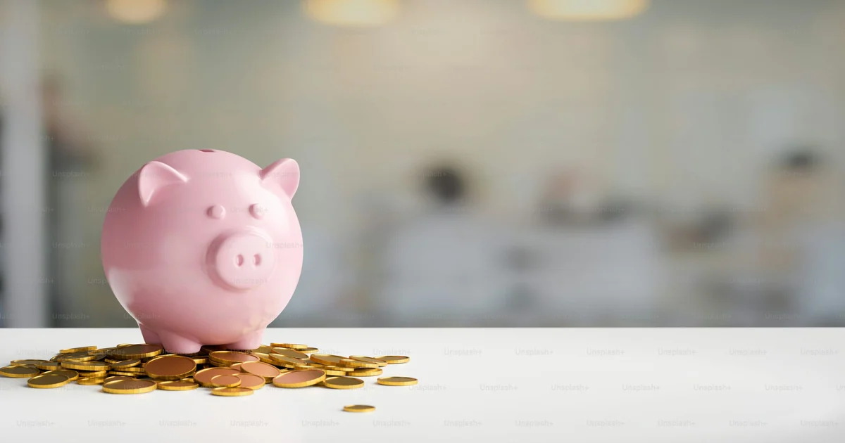 Cofrinho de porquinho rosa sobre moedas espalhadas